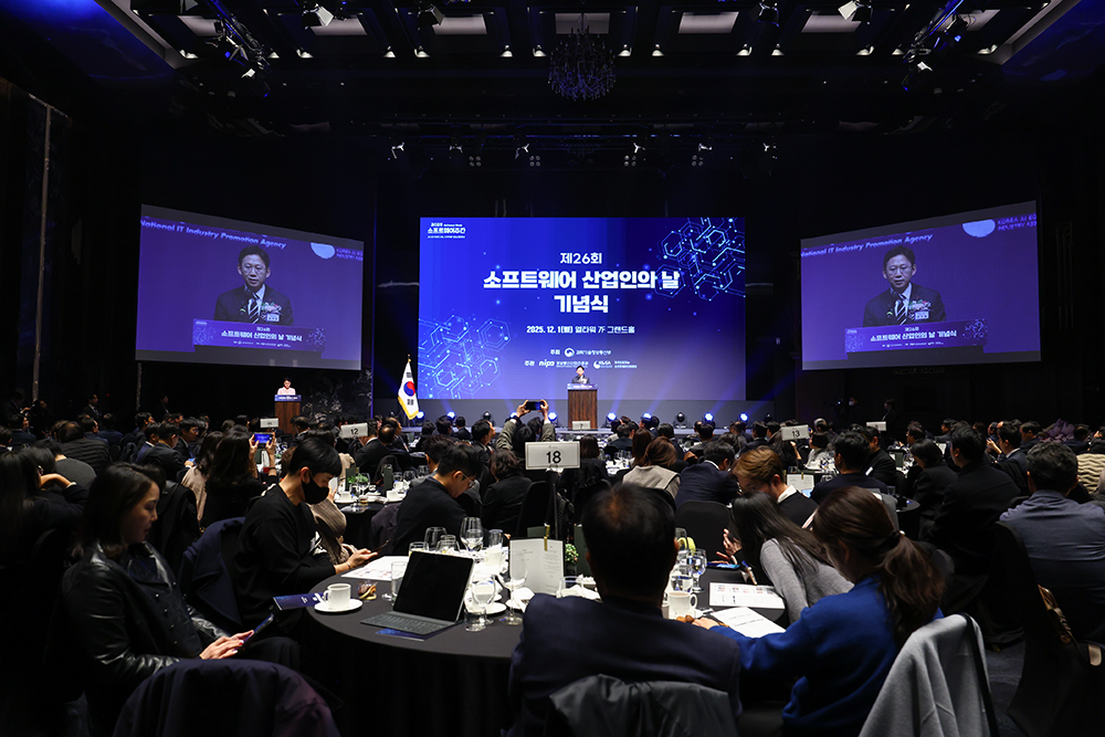 第26回ソフトウェア産業人の日記念式典の会場全景。2025年12月1日、エルタワー7階グランドホールで開催され、大型スクリーンに式典タイトルが映し出されている